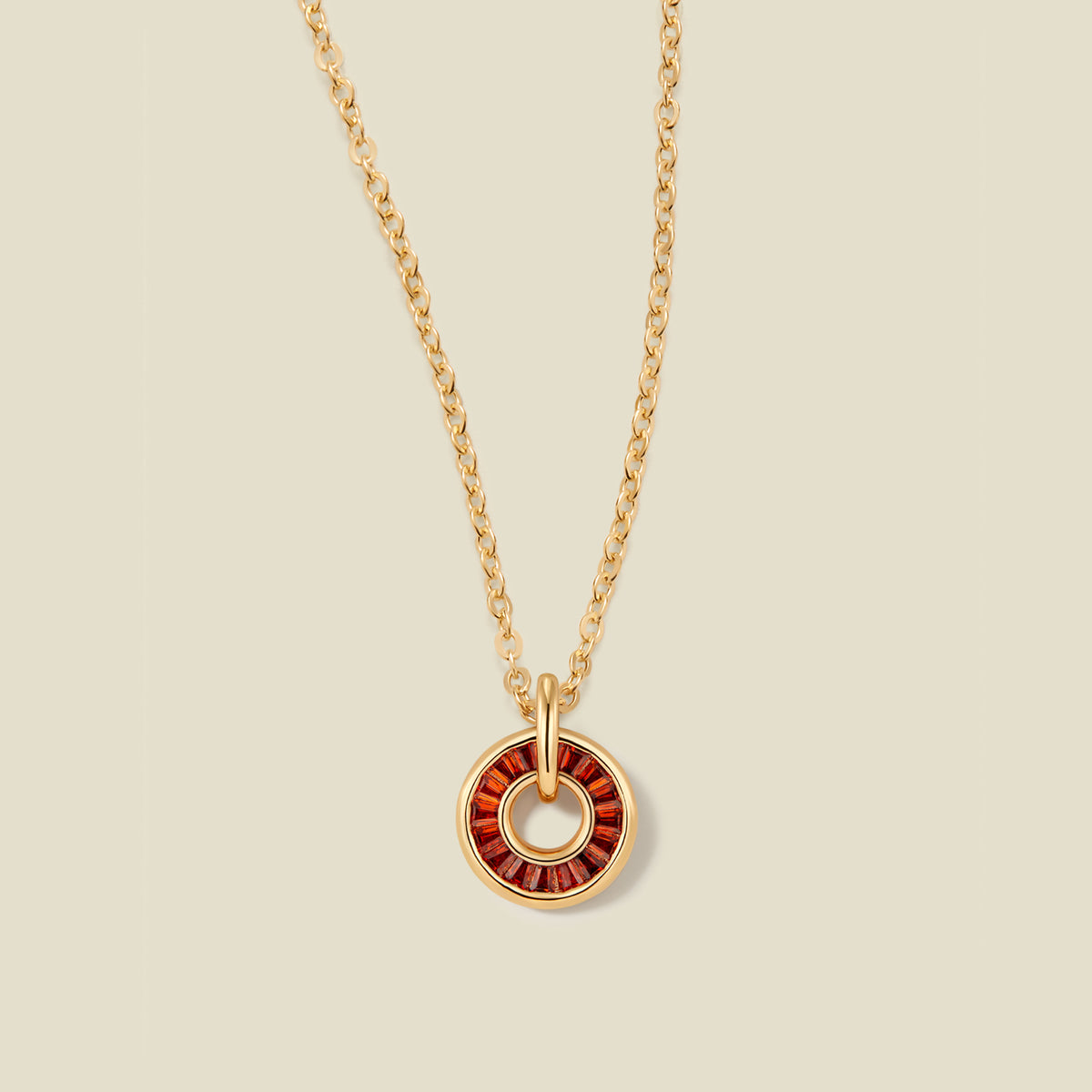 A gold chain necklace with a circular pendant featuring red baguette-cut stones around a hollow center, displayed against a solid light beige background.