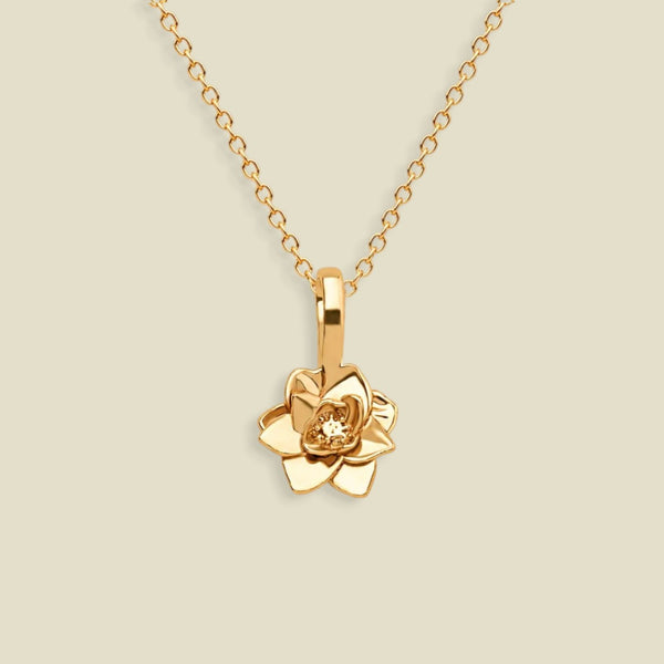 A gold pendant necklace featuring a stylized lotus flower charm, suspended from a delicate gold chain against a solid light beige background.