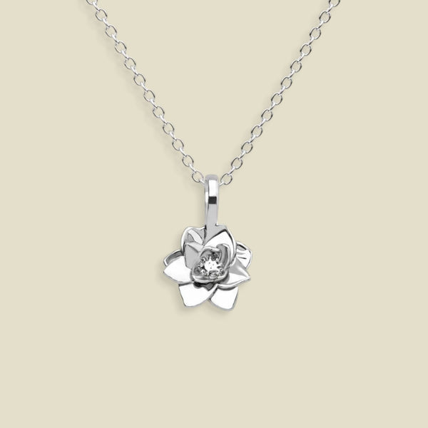 A silver pendant necklace featuring a stylized lotus flower charm, suspended from a delicate silver chain against a solid light beige background.