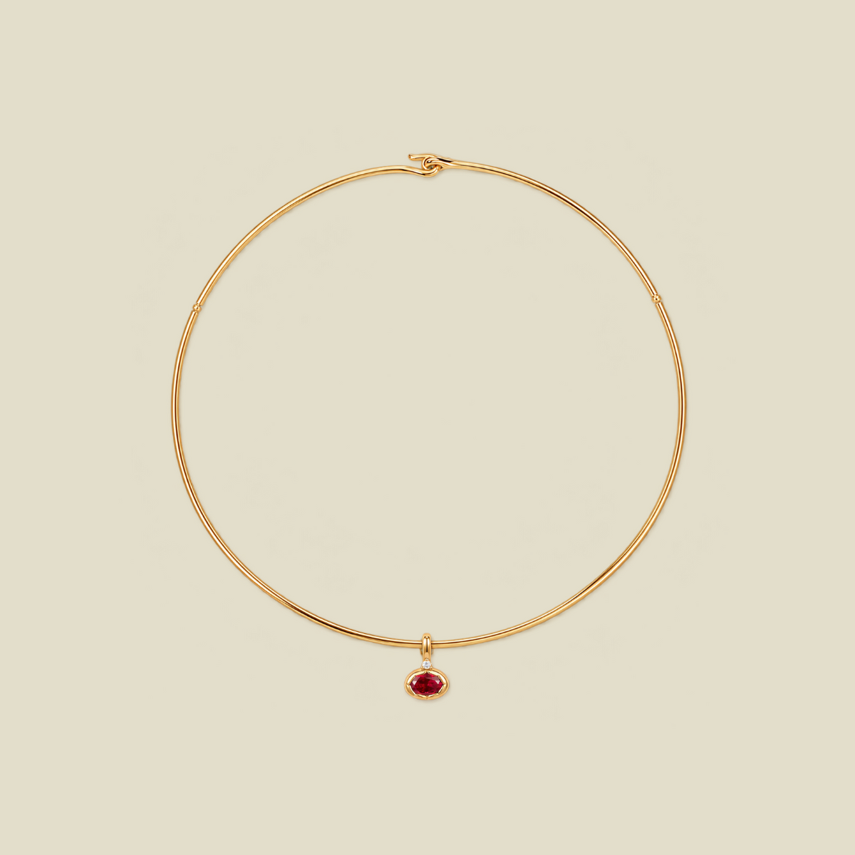 A delicate gold wire choker necklace with a small teardrop-shaped red gemstone pendant, displayed on a solid light beige background.