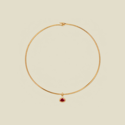 A delicate gold wire choker necklace with a small teardrop-shaped red gemstone pendant, displayed on a solid light beige background.