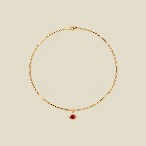 A delicate gold wire choker necklace with a small teardrop-shaped red gemstone pendant, displayed on a solid light beige background.