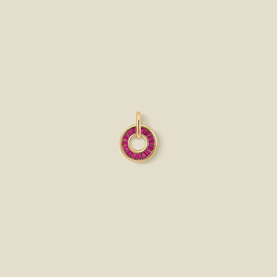 A circular gold pendant featuring red baguette-cut stones around a hollow center, displayed against a solid light beige background.