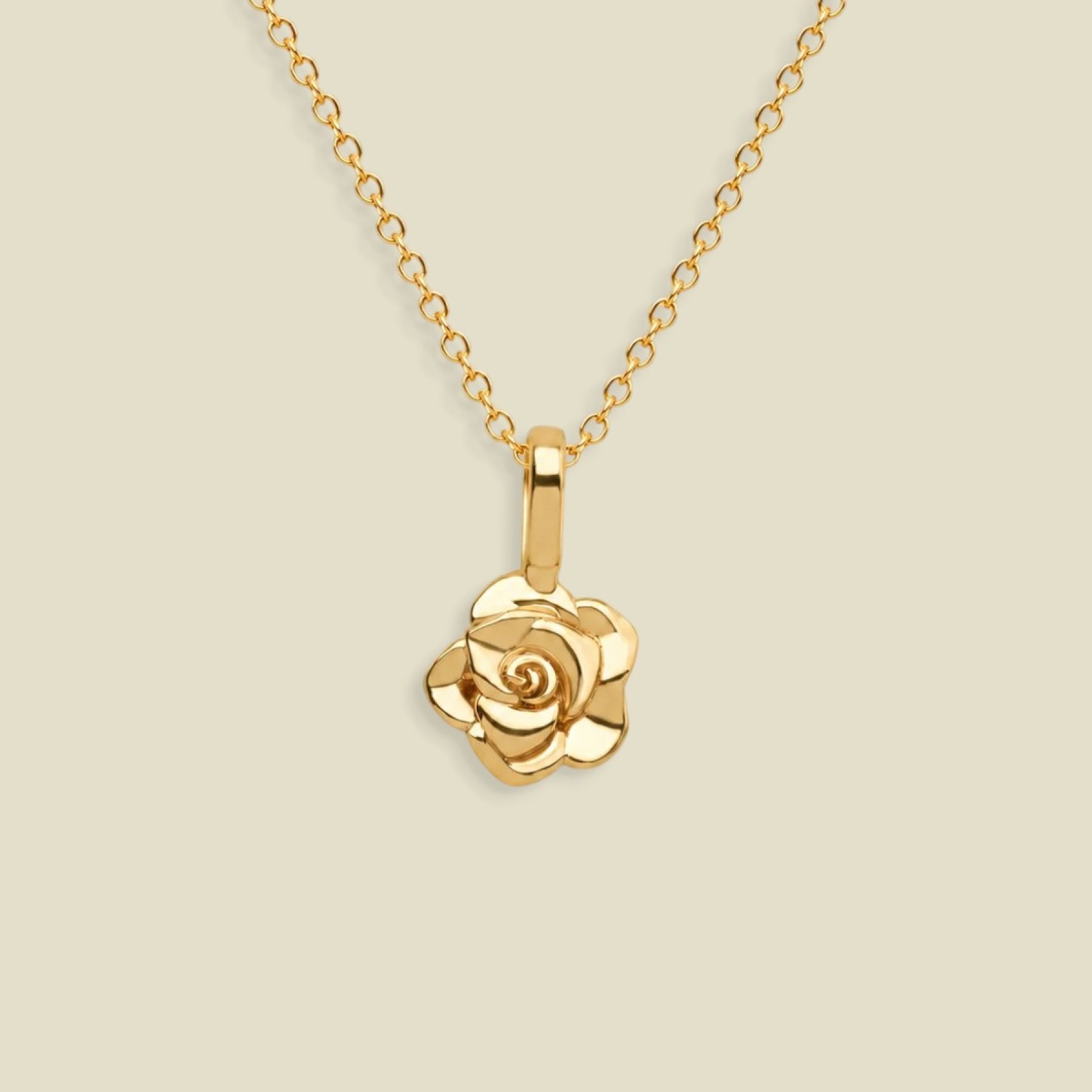 A gold rose pendant necklace on a delicate gold chain, set against a solid light beige background.