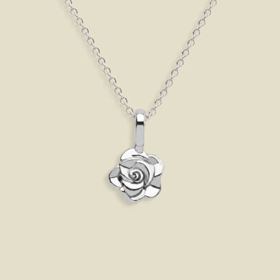 A silver rose pendant necklace on a delicate silver chain, set against a solid light beige background.