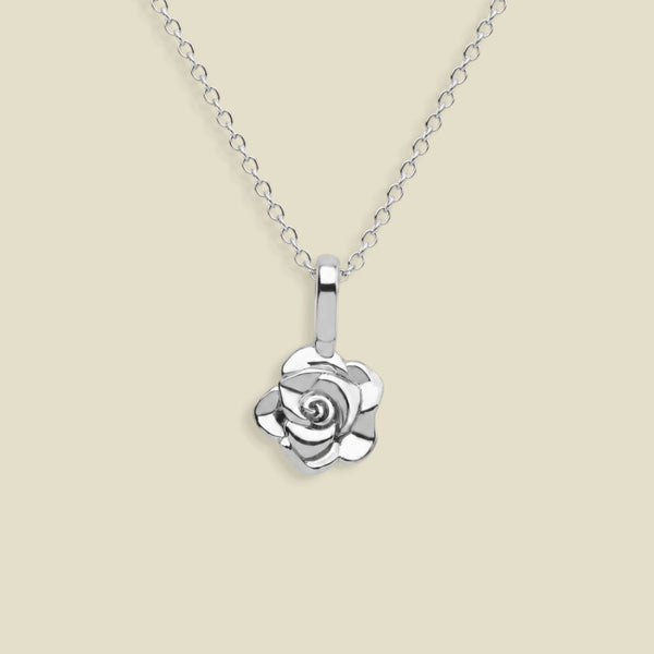 A silver rose pendant necklace on a delicate silver chain, set against a solid light beige background.