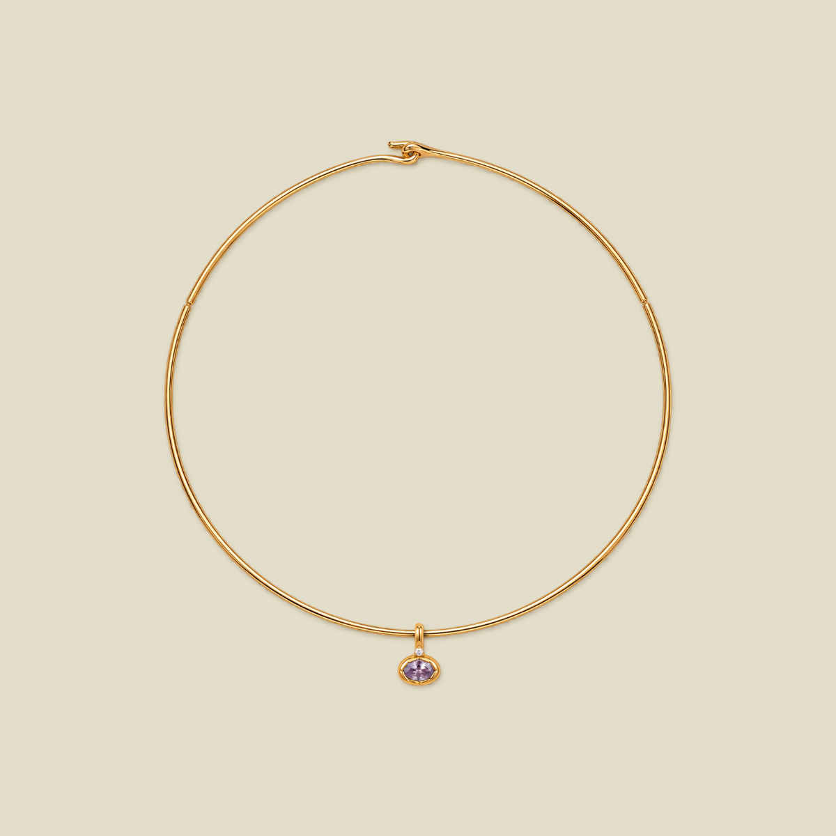 A delicate gold wire necklace with a small dangling charm featuring a light purple oval gemstone, set against a solid beige background.