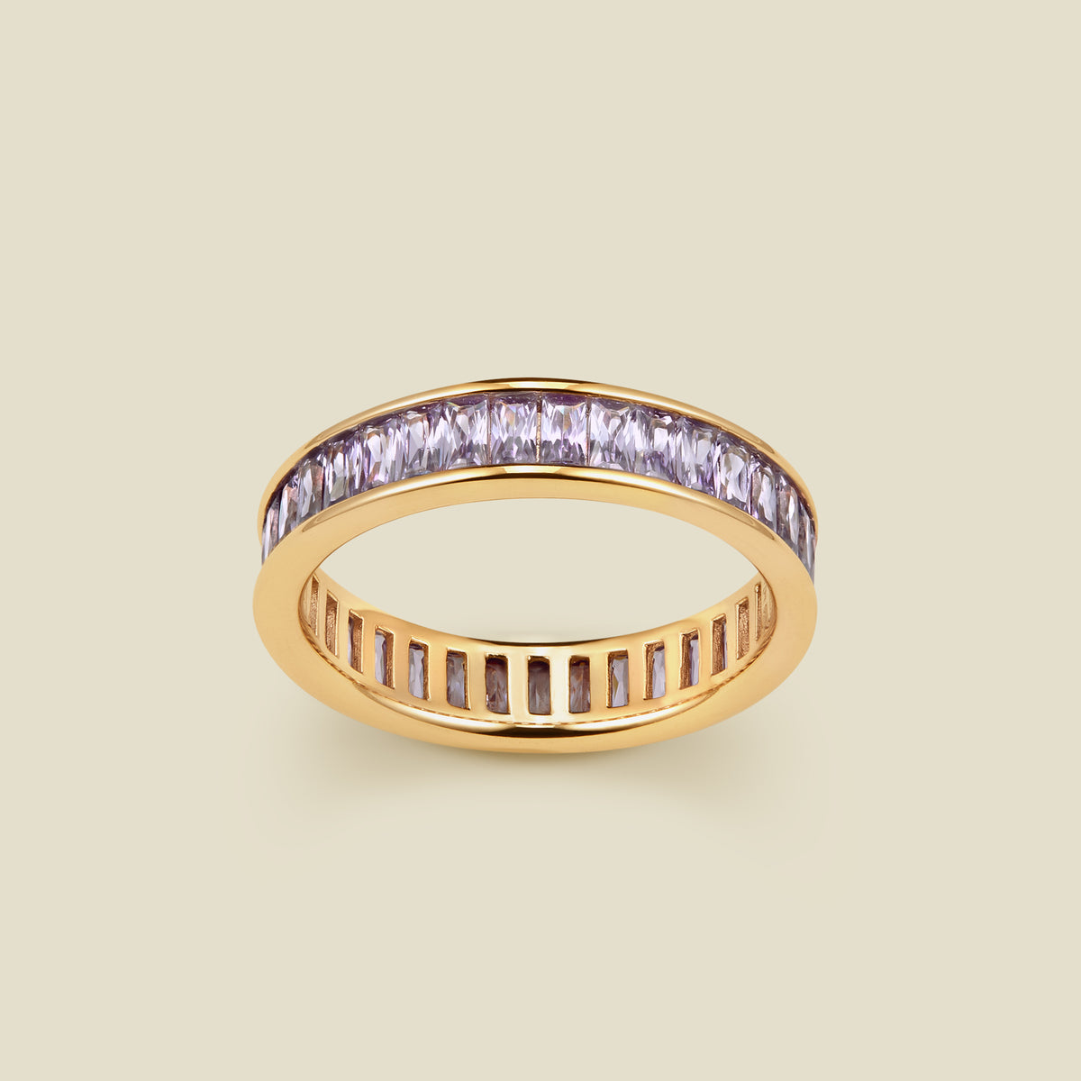 A gold eternity ring featuring a continuous channel setting of baguette-cut light purple gemstones, shown on a solid light beige background.