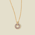A gold chain necklace with a circular pendant featuring light purple baguette-cut stones around a hollow center, displayed against a solid light beige background.