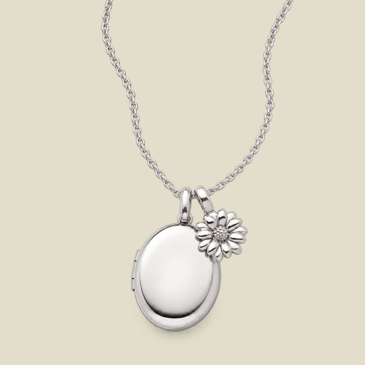 A silver locket necklace with an oval locket and a small daisy flower charm, displayed on a light beige background.