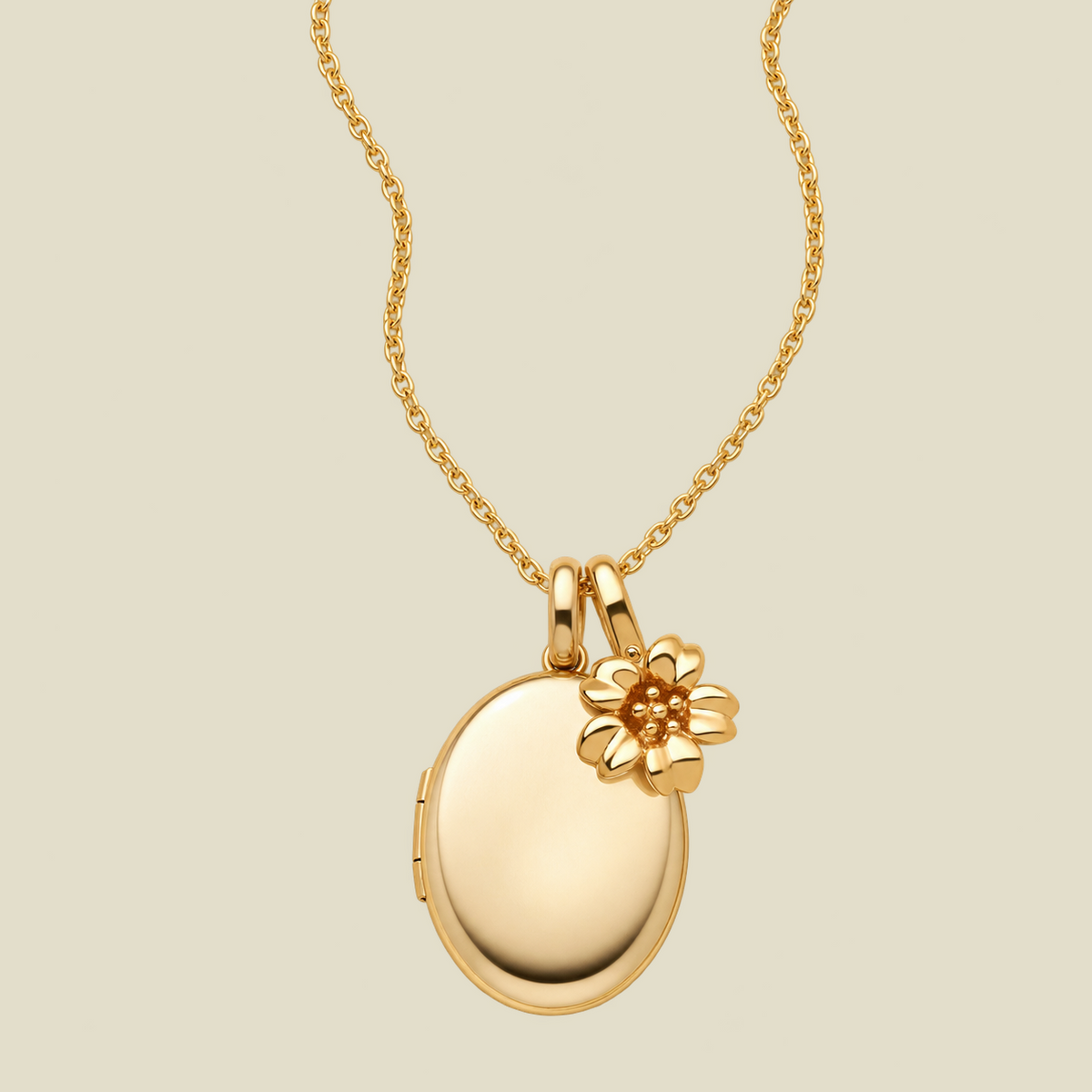 A gold locket necklace with an oval pendant and a small cherry blossom flower charm, shown on a light beige background.