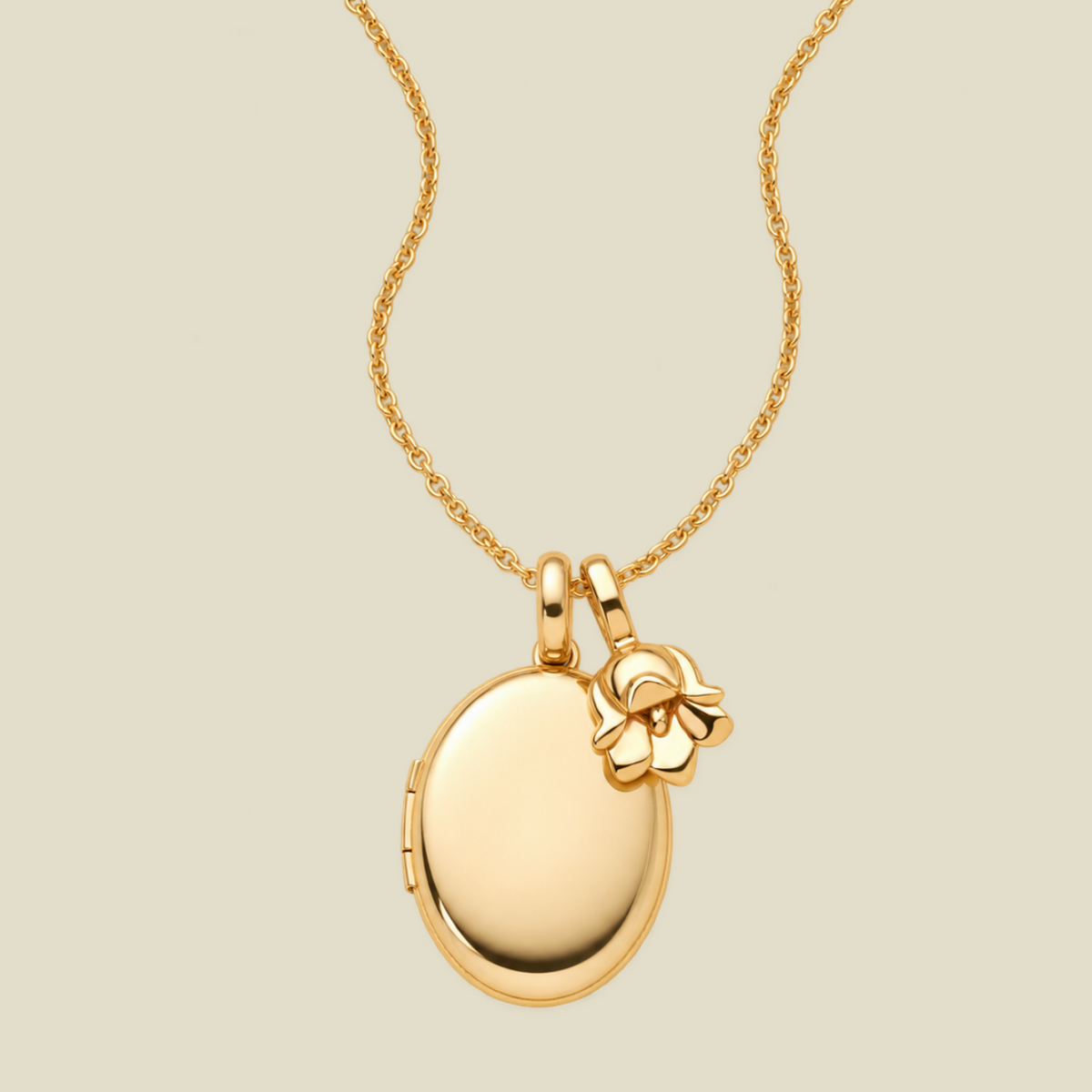 A polished gold locket necklace with a small lily of the valley flower charm, displayed on a light beige background.