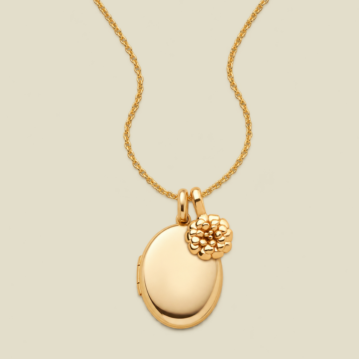 A gold locket necklace featuring a polished oval locket pendant with a textured floral charm, suspended from a delicate gold chain against a solid light beige background.