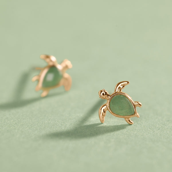 Gold turtle-shaped earrings on a light green background