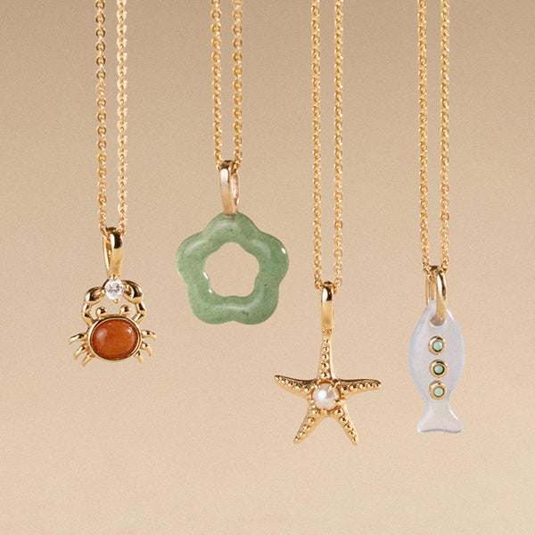 Four gold necklaces with various colored pendants on a beige background