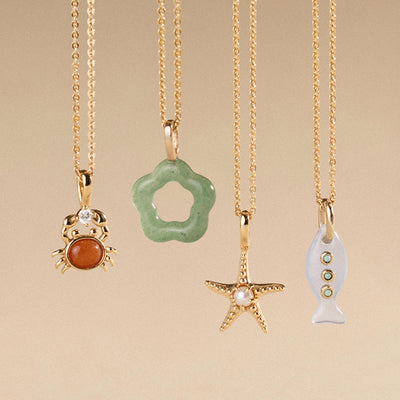Four gold necklaces with various shaped and colored pendants on a beige background