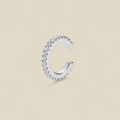 A silver-toned C-shaped huggie hoop ear cuff encrusted with clear cubic zirconia stones, shown on a solid beige background.