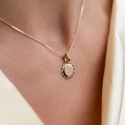 Gold necklace with disc charm engraved with the letter "e" and green stone charm on a model