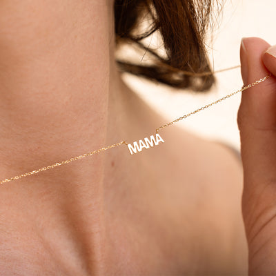 Close-up of a woman holding a delicate gold necklace with a pendant that spells “MAMA".