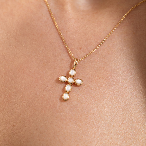 Close-up of a gold necklace with a cross pendant made of bezel set pearls, resting on the wearer’s chest.