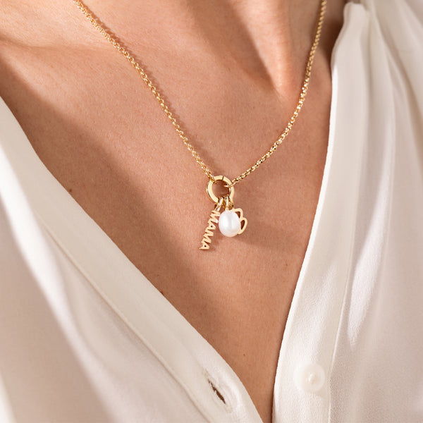 Gold necklace with a pearl charm, Script B Charm and 'MAMA' charm on a white shirt.