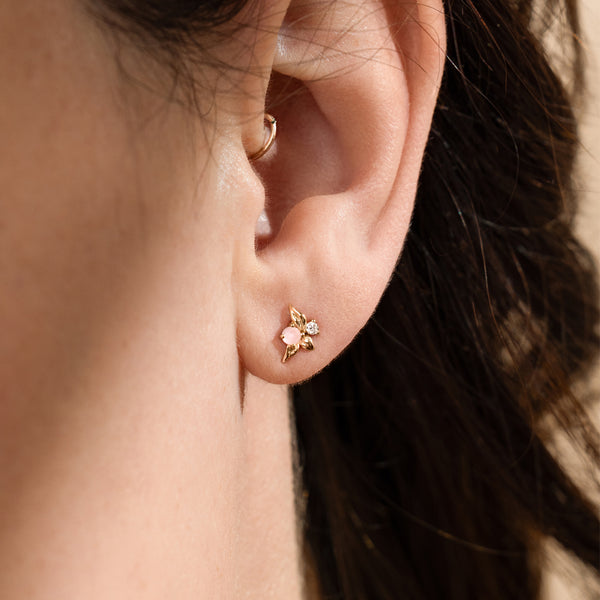 Close-up of a woman's ear wearing gold studs with a pink prong-set stone.