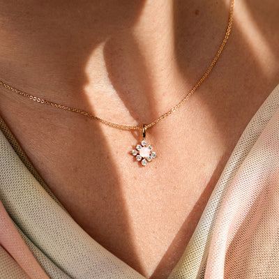 Close-up of a person wearing a pink and clear stone pendant on a gold chain. 
