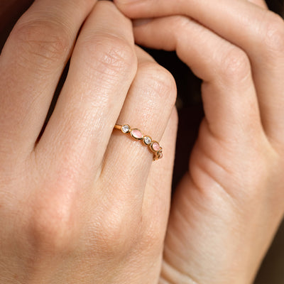 Close-up of a person's hands wearing a gold ring with pink and clear bezel-set stones.