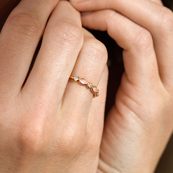 Close-up of a person's hands wearing a gold ring with pink and clear bezel-set stones.