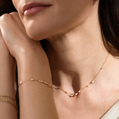 Close-up of a woman wearing a pink bezel-set stone necklace, and gold bracelets.
