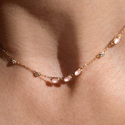 Close-up of a person wearing a gold necklace with pink bezel-set stones. 