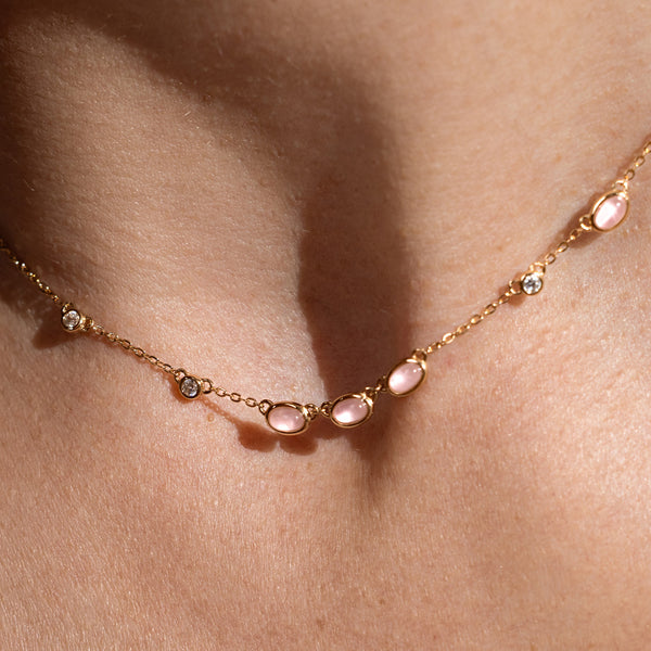 Close-up of a person wearing a gold necklace with pink bezel-set stones. 