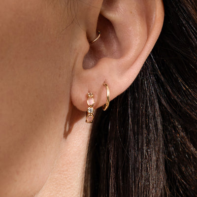 Close-up of a woman's ear wearing gold hoops with pink bezel-set stones paired with a second gold hoop.