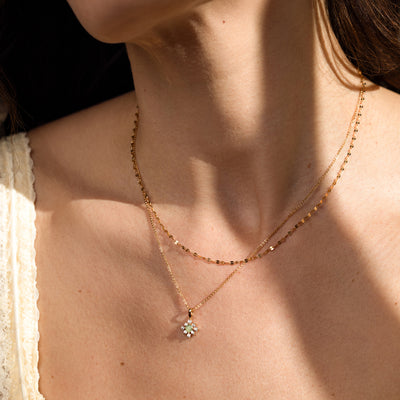 Close-up of woman wearing a green stone pendant on a gold chain, layered with a lace chain necklace.