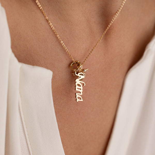 Gold necklace with 'Nana' pendant on a person wearing a white top.