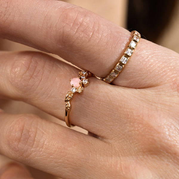 Close-up of a hand wearing two gold rings with clear and pink stones.