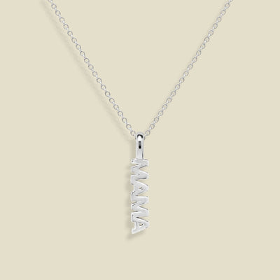 A silver name necklace featuring a vertical pendant spelling 'MAMA' in an openwork design, suspended from a delicate silver cable chain against a solid beige background.