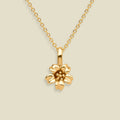 A gold cherry blossom flower pendant necklace on a delicate gold chain, set against a solid light beige background.