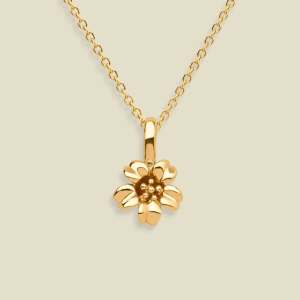 A gold cherry blossom flower pendant necklace on a delicate gold chain, set against a solid light beige background.