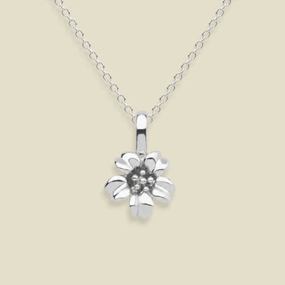 A silver cherry blossom flower pendant necklace on a delicate silver chain, set against a solid light beige background.