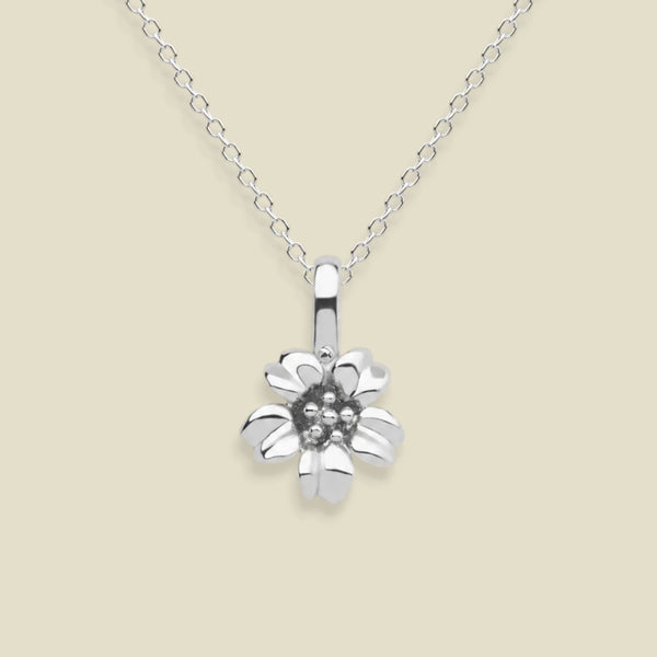 A silver cherry blossom flower pendant necklace on a delicate silver chain, set against a solid light beige background.