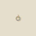 A gold circular pendant featuring light blue baguette-cut stones around a hollow center, displayed against a solid light beige background.