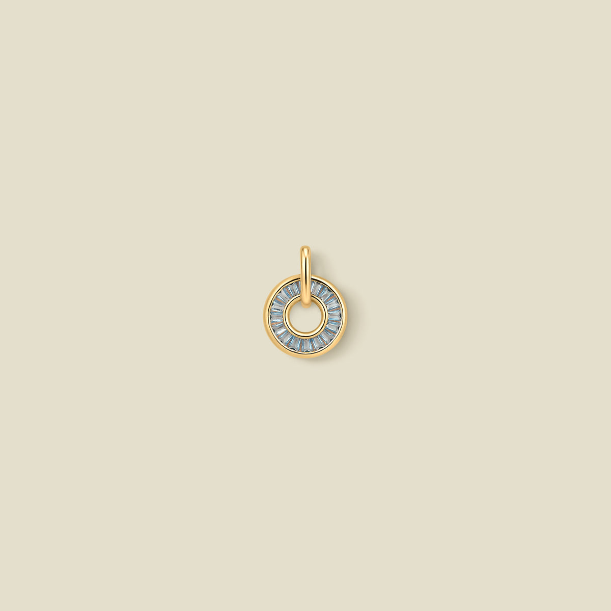A gold circular pendant featuring light blue baguette-cut stones around a hollow center, displayed against a solid light beige background.