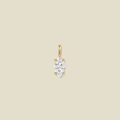 A single gold pendant featuring a marquise-cut clear gemstone in a prong setting, centered on a solid beige background.