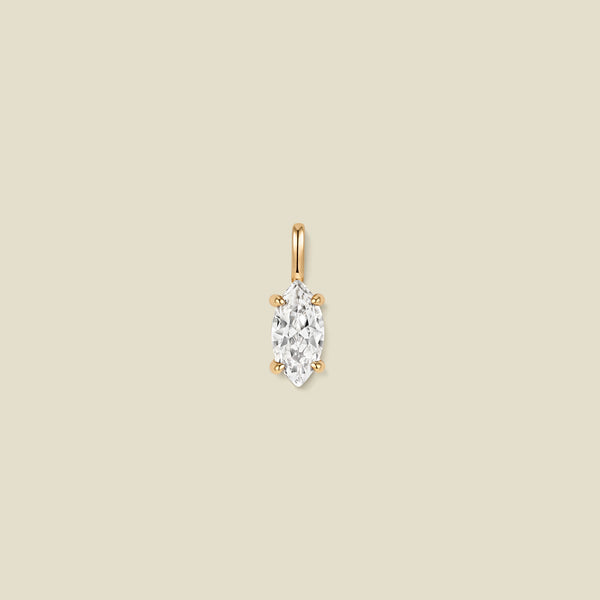 A single gold pendant featuring a marquise-cut clear gemstone in a prong setting, centered on a solid beige background.