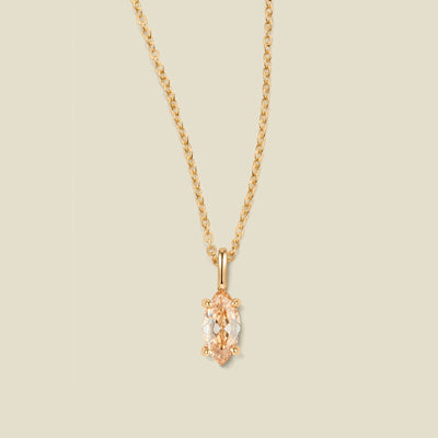 A delicate gold chain necklace with a small gold pendant featuring a central warm golden marquise-cut gemstone, set against a solid light beige background.