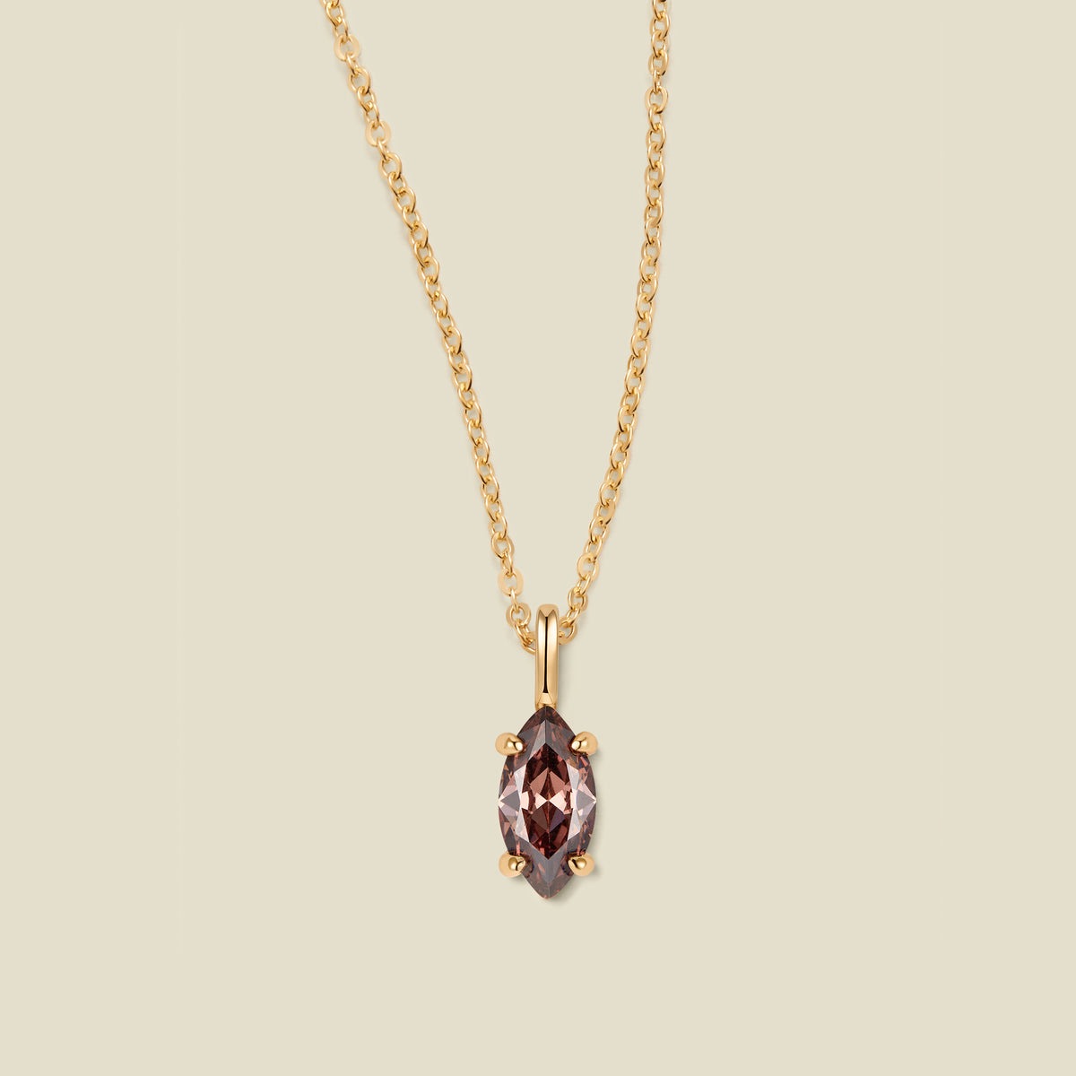 A gold chain necklace with a marquise-cut dark brown/black gemstone pendant in a gold setting, shown against a solid light beige background.