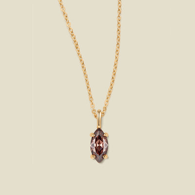 A gold chain necklace with a marquise-cut dark brown/black gemstone pendant in a gold setting, shown against a solid light beige background.