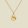 A polished yellow gold necklace with a small lily of the valley flower-shaped pendant, displayed against a solid light beige background.