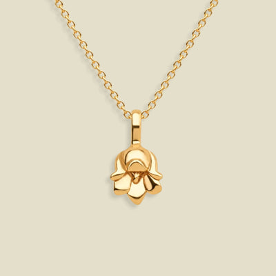 A polished yellow gold necklace with a small lily of the valley flower-shaped pendant, displayed against a solid light beige background.